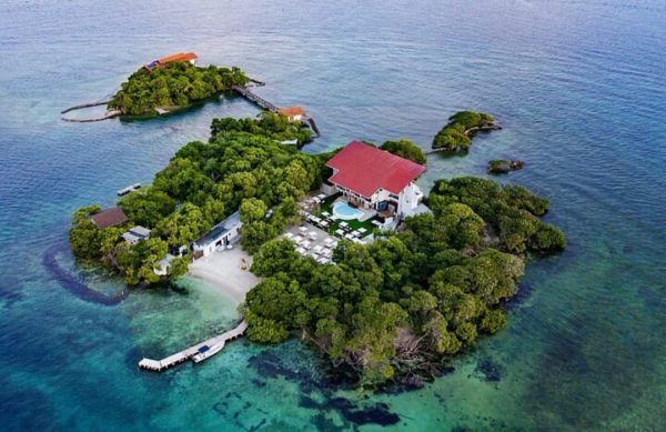 Vista aérea de un resort tropical en una isla con techo rojo y un bote blanco cerca
